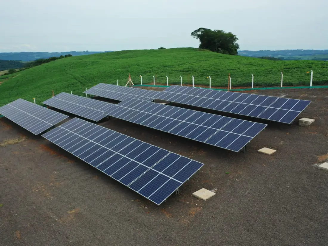 Usina fotovoltaica em solo com quatro fileiras de mesas, cercada por área de plantio