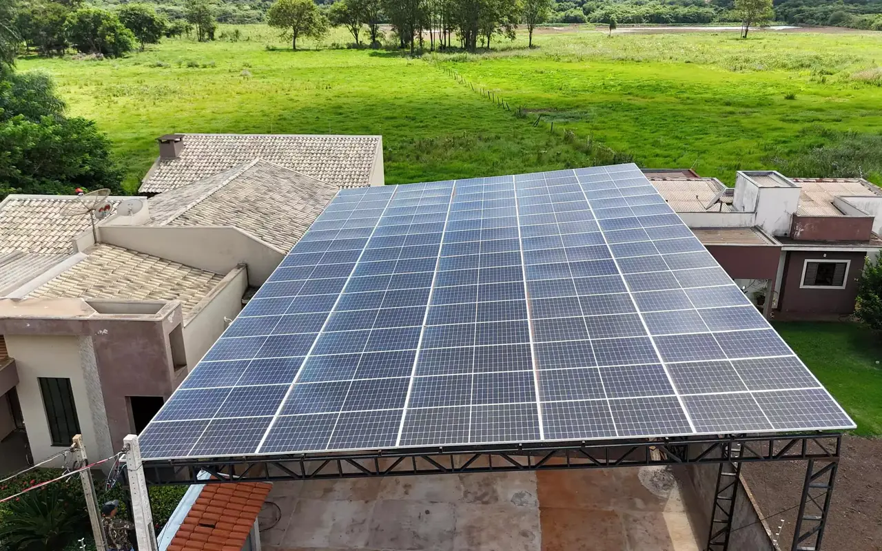 Estrutura metálica em propriedade rural coberta por módulos fotovoltaicos, com pastagem ao fundo